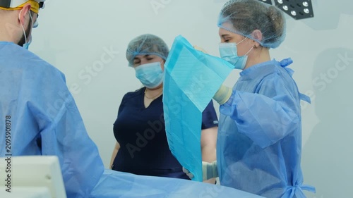 Experienced surgeon performs complex surgical procedure. Concentrated women nurses assist in bright sterile operating room. Slow motion