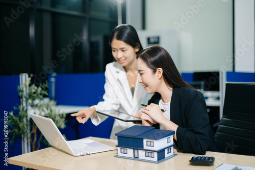 Professional Asian real estate consultant presenting a house model to a client during a property investment meeting in a modern office.