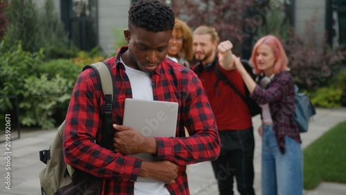 Upset African American guy male student bullied man feeling despair bullying by multiracial students bad gossiping showing thumb down judge disrespect teasing mocking bully at city college university