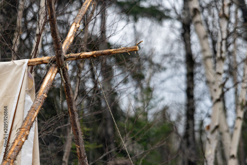 Fotografi Parents, Quebec, 19 May 2026 : Rustic wooden structure made of branches tied together supports a piece of fabric in a forest