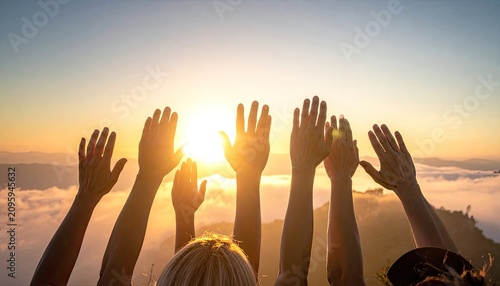 Group of diverse hands reaching up towards the sun at sunrise over clouds.