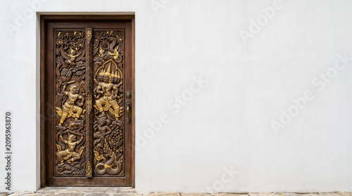 Intricately carved Thai wooden door with mythological figures on a minimalist wall with copy space
