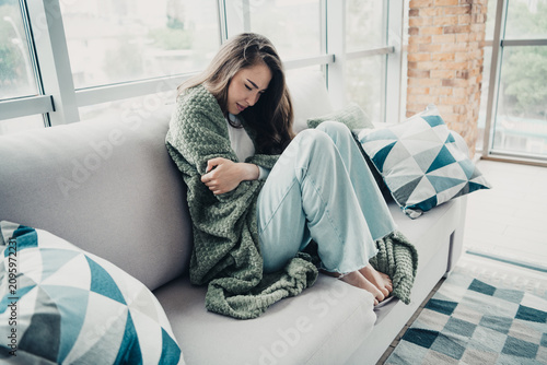 Картината върху платно Young woman feeling unwell at home wrapped in a blanket on a sofa looking distre