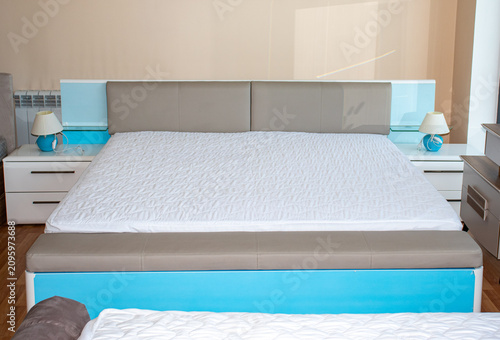 Fotografía Modern king size double bed with white mattress and turquoise frame displayed with nightstands and lamps in a furniture showroom interior front view