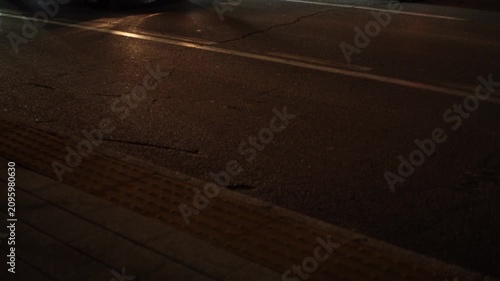 Side view Video of evening city street with paved road, cars in lanes separated by markings. Sidewalk is equipped with raised lines to assist visually impaired or blind pedestrians with orientation
