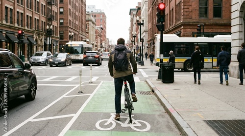 Man rides bicycle on bike lane alongside busy city street with cars and bus