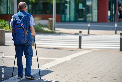 Full length rear view of a senior man wearing a denim vest and backpack while using Nordic walking poles on a sunny sidewalk, Gdynia, Pomerania, Poland, Europe
