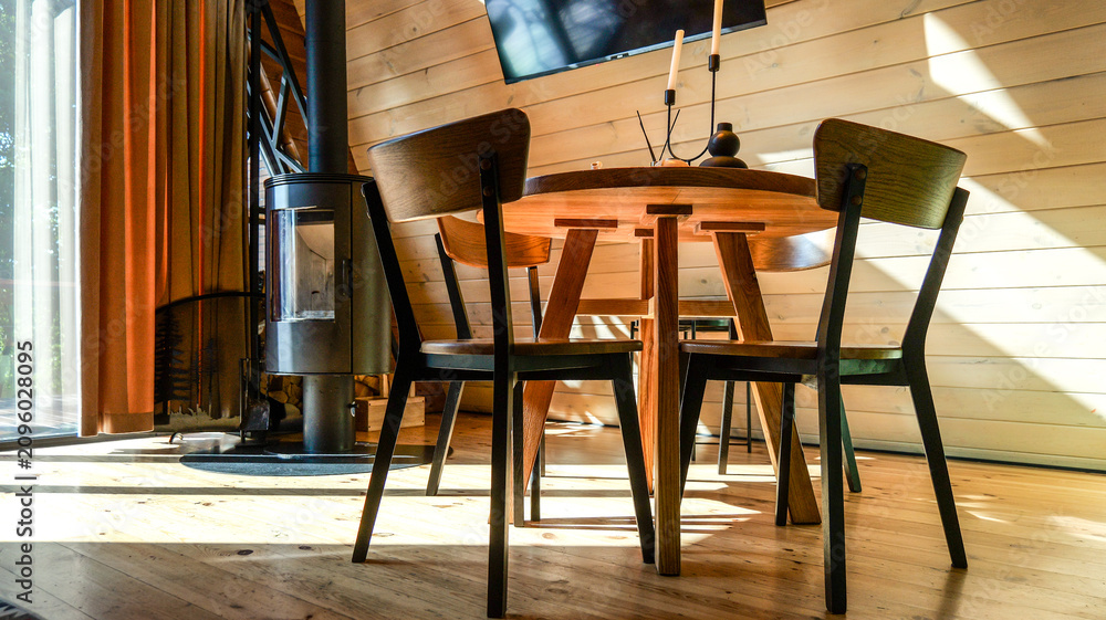 Obraz premium Cozy dining area with modern wood table and chairs next to a sleek wood-burning stove