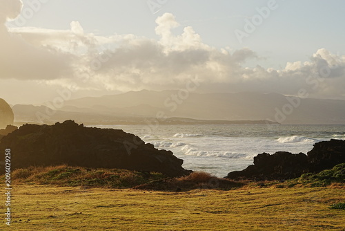 Fotografie Volcanic coast with lava rocks and ocean waves in golden evening haze, Sao Migue