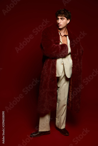 Elegant young man showcases bold fashion in a striking pose against a deep red backdrop