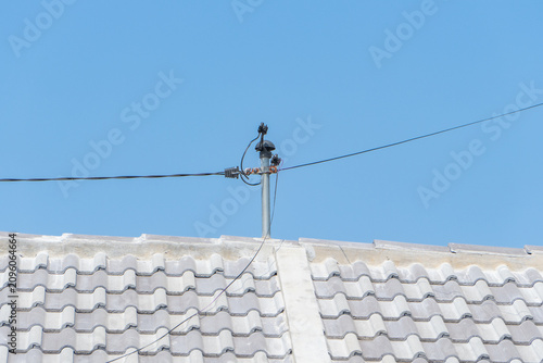 Domestic electrical wire connection on house rooftop against clear blue sky background