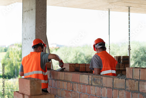 Skilled builders lay bricks spreading mortar with trowel at construction site. Experienced construction workers perform meticulous brickwork