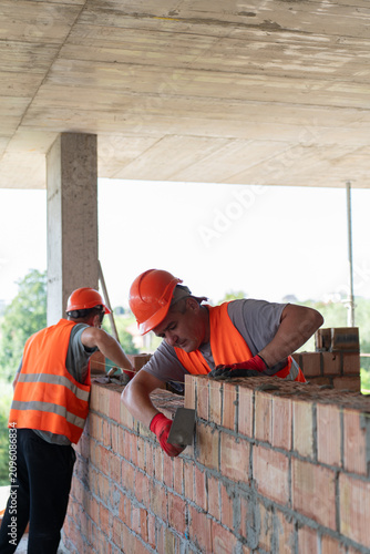 Workers take away unnecessary mortar from brick joints to maintain quality construction. Builders clean construction lines with tools. Vertical shot