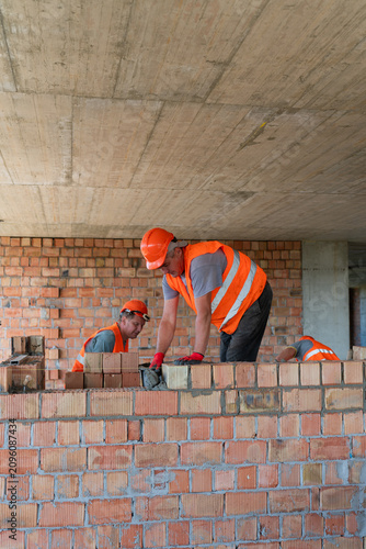 Men workers spread mortar with trowels and place bricks precisely into positions to create wall. Builders observe alignment of walls. Vertical shot