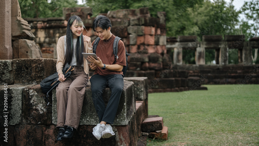 Obraz premium Young Asian Travelers Reviewing Digital Map While Resting at Historic Temple