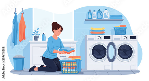 Young housewife kneeling on the floor and folding clean clothes in a laundry room with modern washing machines and dryer.