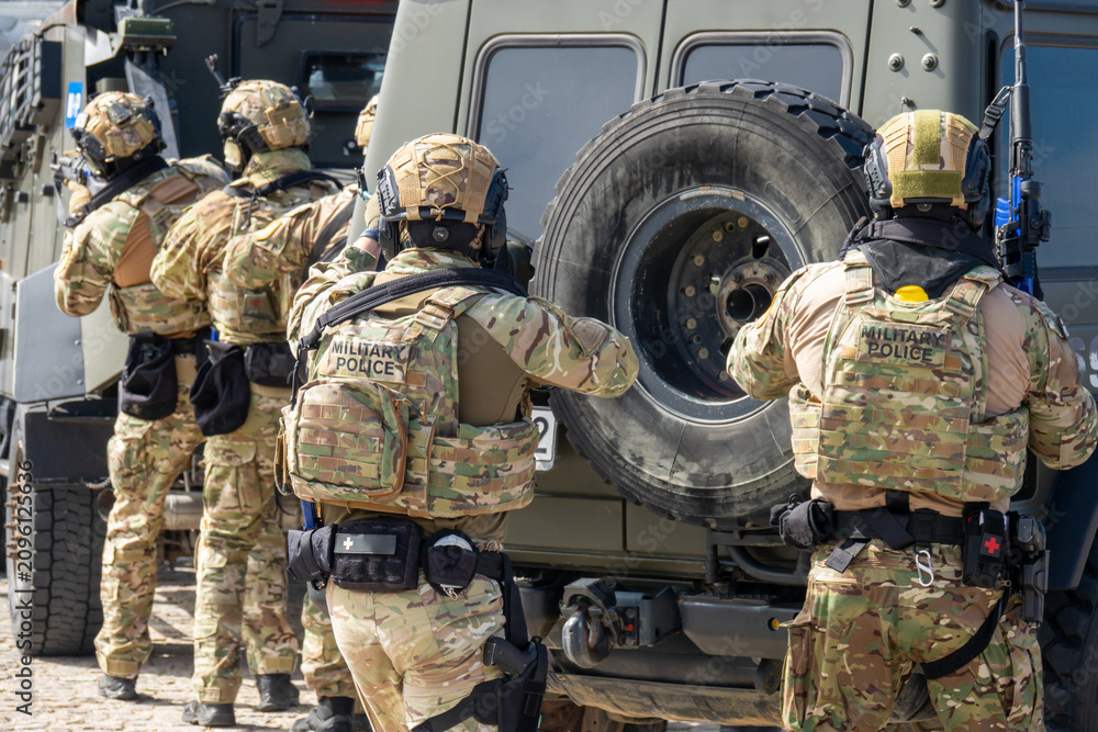 Fototapeta premium Armed Special Forces Soldiers in Camouflage Tactical Gear Storming Armored Vehicle During Military Training Exercise or Combat Operation