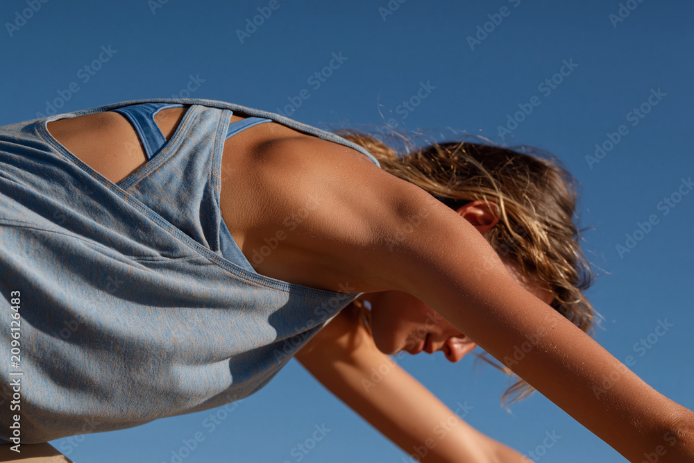 Fototapeta premium Serene yoga woman stretching in cat cow pose under clear blue sky, close up of torso arm and shoulder showing athletic top and relaxed focus