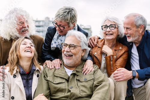 Diverse group of senior friends laughing and embracing in a retirement community, enjoying outdoor leisure, connection, and joyful, authentic moments of friendship and well-being