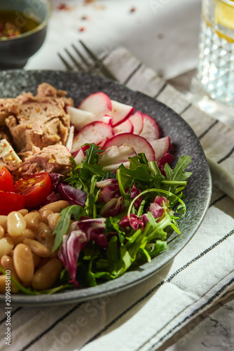 Healthy Mediterranean salad with canned tuna, white beans, feta cheese, cherry tomatoes, and greens on a stone plate.