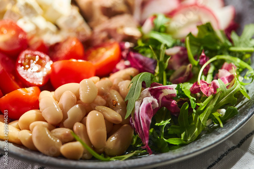 Healthy Mediterranean salad with canned tuna, white beans, feta cheese, cherry tomatoes, and greens on a stone plate.