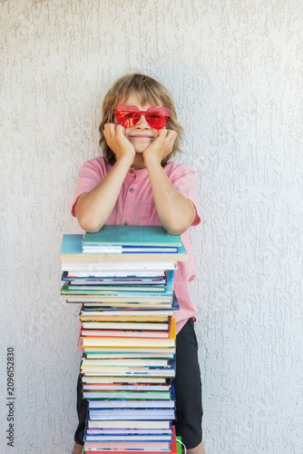 concept of learning with pleasure. happy schoolchild wearing heart-shaped glasses next to a tall stack of books. Personal growth, a love for reading and book recommendations, path to success.