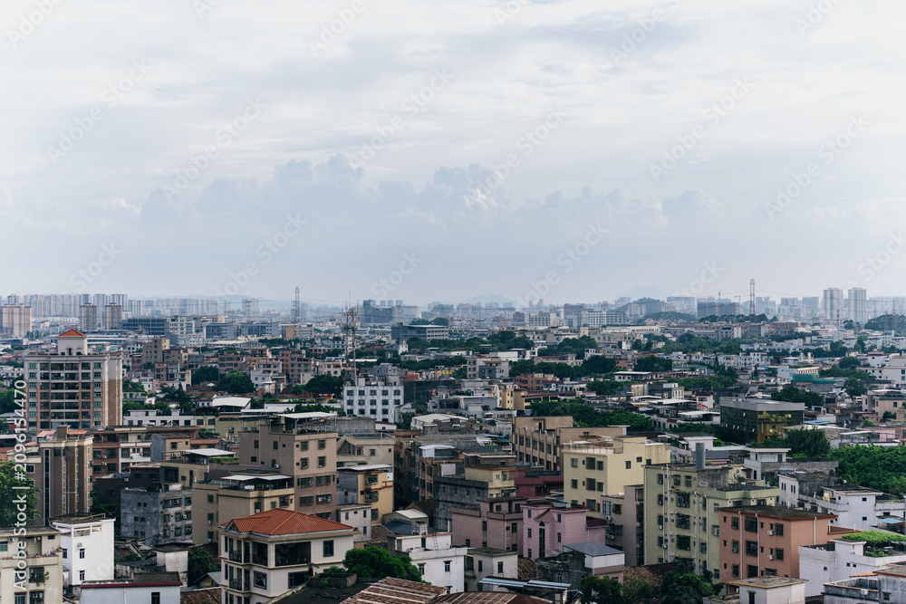 Fototapeta premium Cityscape of dense urban neighborhood with multi-story buildings under cloudy sky, distant skyline visible in background
