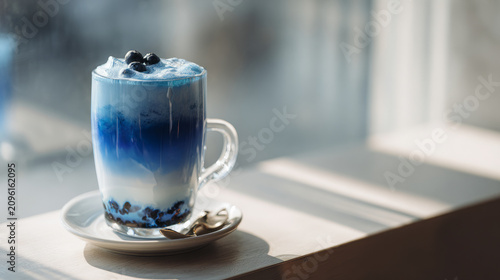 Chilled blue drink served in a glass with a creamy top and fresh blueberries on a bright sunny table