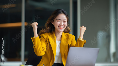 Happy young woman celebrating her achievements while working on a laptop in a contemporary office environment