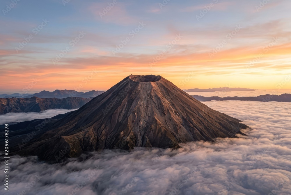 Fototapeta premium Volcano peak above clouds at sunrise with dramatic sky