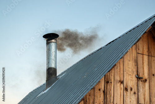 Dark smoke billowing from a metal chimney on a wooden roof