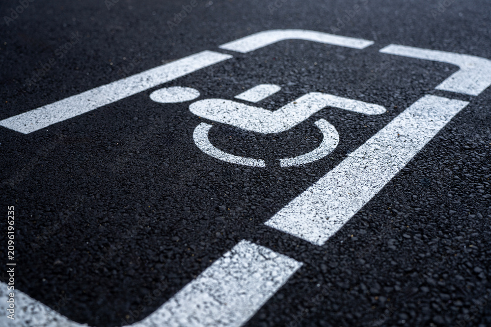Obraz premium White painted disabled parking space symbol on dark asphalt surface close up.