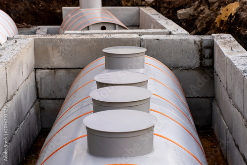 Underground plastic septic tanks with round manhole covers installed inside a concrete foundation pit at a construction site, illustrating sewage systems and waste management.