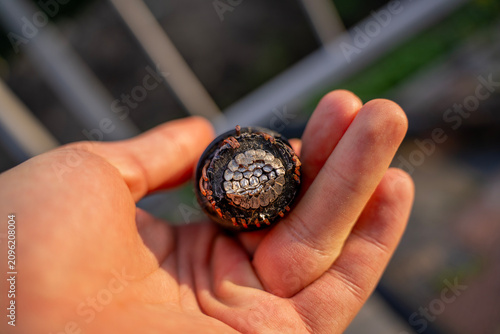 Male hand holding a cut thick power cable showing the multi wire aluminum and copper conductor cross section  industrial electrical engineering and utility infrastructure concept.