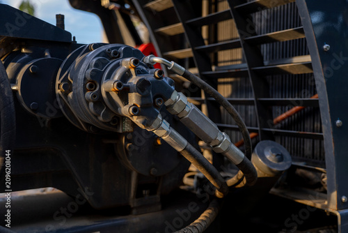 Hydraulic pump engine mechanism with high pressure flexible hoses connected to the block, heavy machinery engine compartment with radiator grill background.