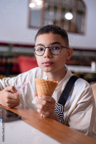A young boy of Middle Eastern descent enjoying an ice cream cone at a cozy café.