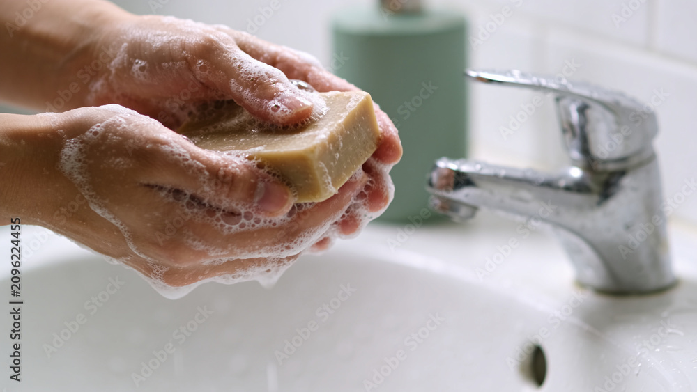 Fototapeta premium Person Washing Hands With Natural Bar Soap at the white sink For Proper Daily Hygiene And Cleanliness