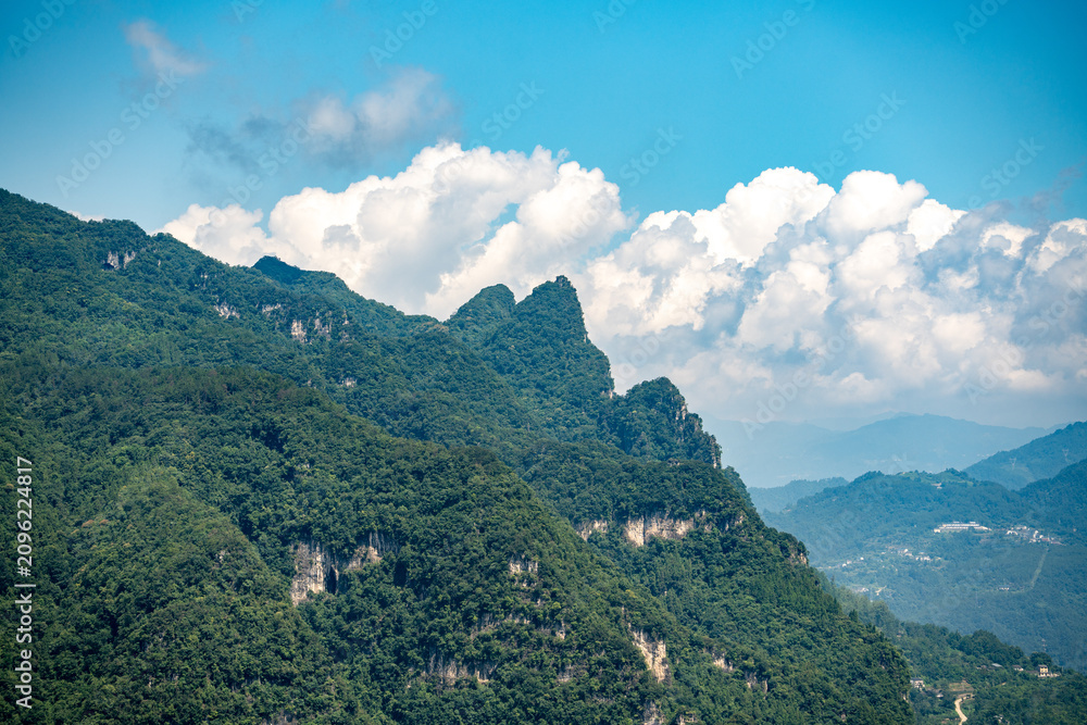 Obraz premium The lush green mountains rise above the Three Gorges Reservoir near Yichang in China under a bright blue sky with white clouds during the summer season