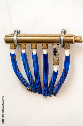 Принти на полотні Brass plumbing manifold with blue corrugated pipes on white wall