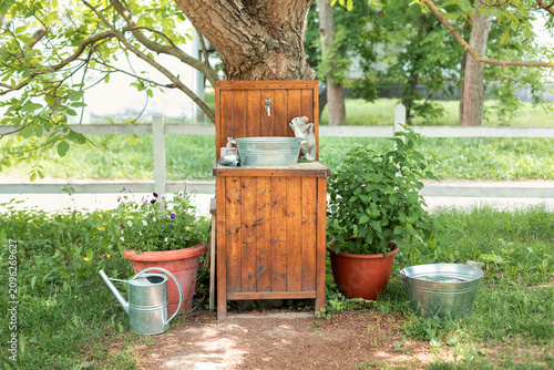Valokuva Rustic wooden garden washstand with metal sink basin and tap standing under a tree in a sunny backyard