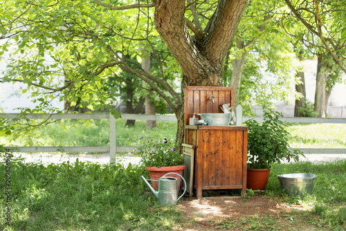 Canvas Print Rustic wooden garden washstand with metal sink basin and tap standing under a tree in a sunny backyard