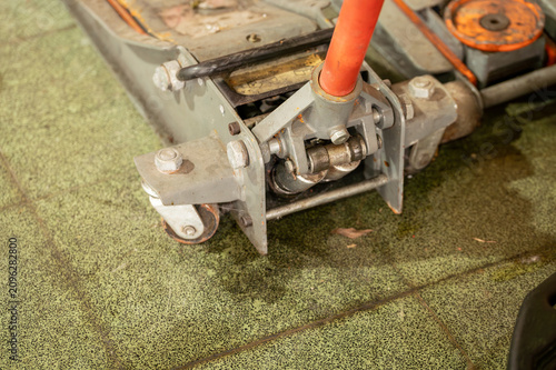Cuadro en lienzo A close-up shot of a professional metallic trolley floor jack with an orange handle mechanism, standing on a textured green industrial tile floor inside an automotive repair shop