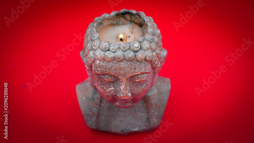 Photography Grey Buddha Head Candle Holder with Lit Candle on a Red Background