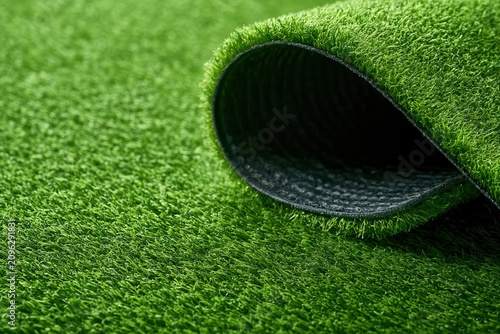 Roll of artificial grass laying on a flat surface showing the texture and color of the material used for outdoor and indoor spaces
