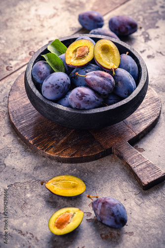Fresh ripe plums in a rustic bowl on a wooden board, a healthy fruit snack