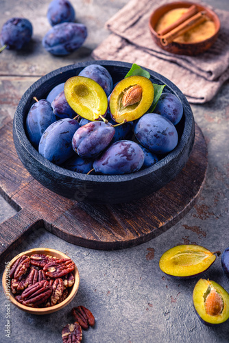 Fresh ripe plums in a rustic bowl on a wooden board, a healthy fruit snack
