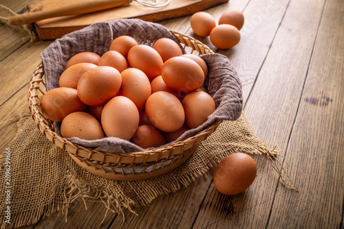 Foto Basket full of fresh brown eggs on a rustic wooden table with a whisk and shell