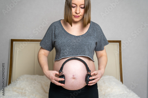Pregnant woman holding headphones against her baby bump, symbolizing prenatal bonding through music during pregnancy. Expectant mother creating a calm and relaxing environment for her unborn baby 