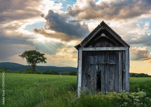 Billede på lærred Abandoned Wooden Hut in Expansive Agricultural Landscape at Sunset with Dramatic