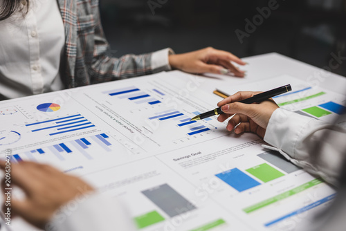 Business team reviewing financial reports, charts, and graphs on paperwork, discussing market strategy.